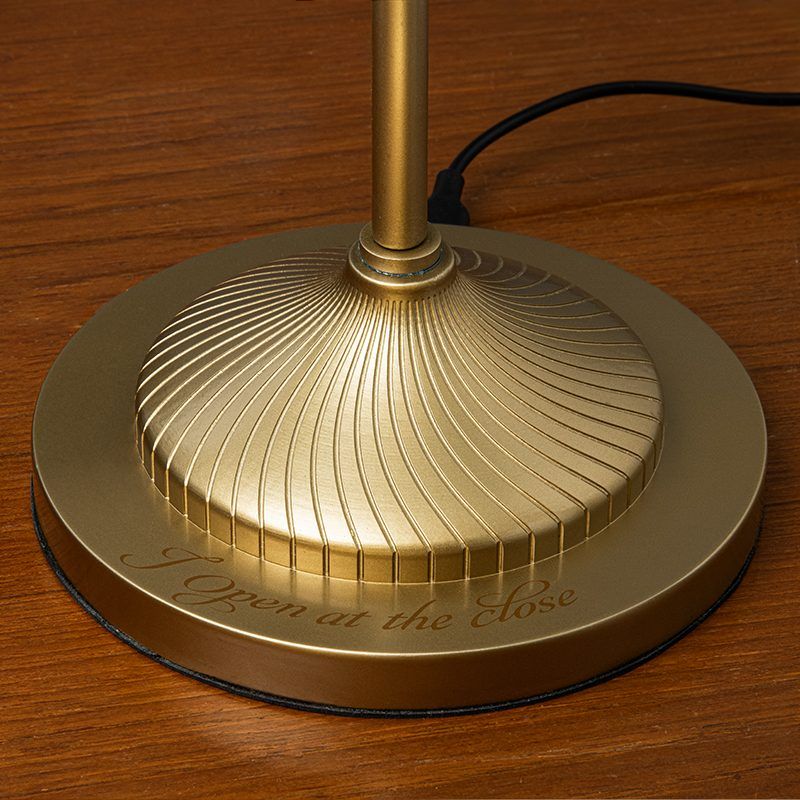 Gold lamp base with 'I Open at the Rose' engraving on a wooden surface