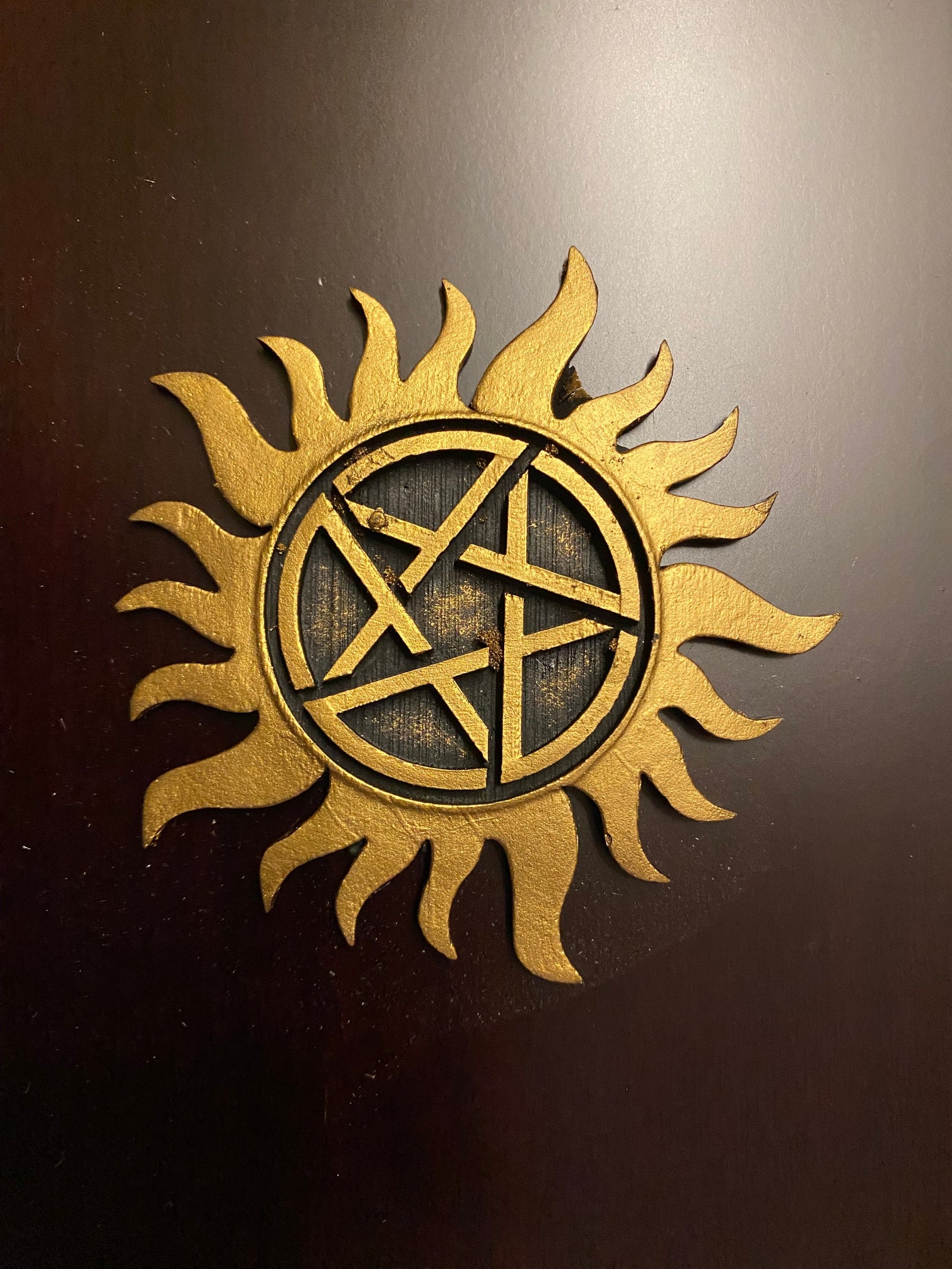 Gold sun-shaped symbol with a pentagram in the center on a dark background