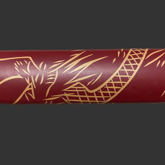 Maroon cylindrical object with gold leaf patterns on a dark background