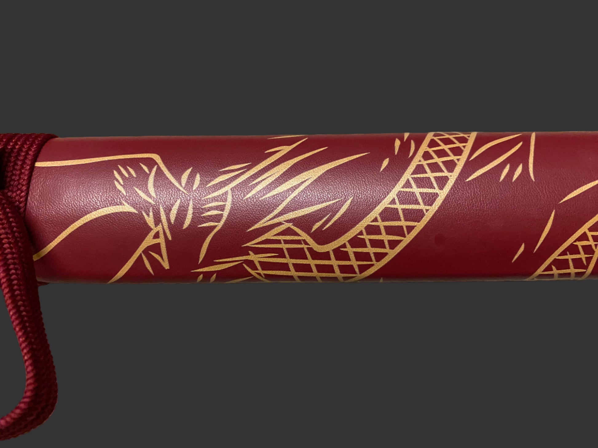 Maroon cylindrical object with gold leaf patterns on a dark background