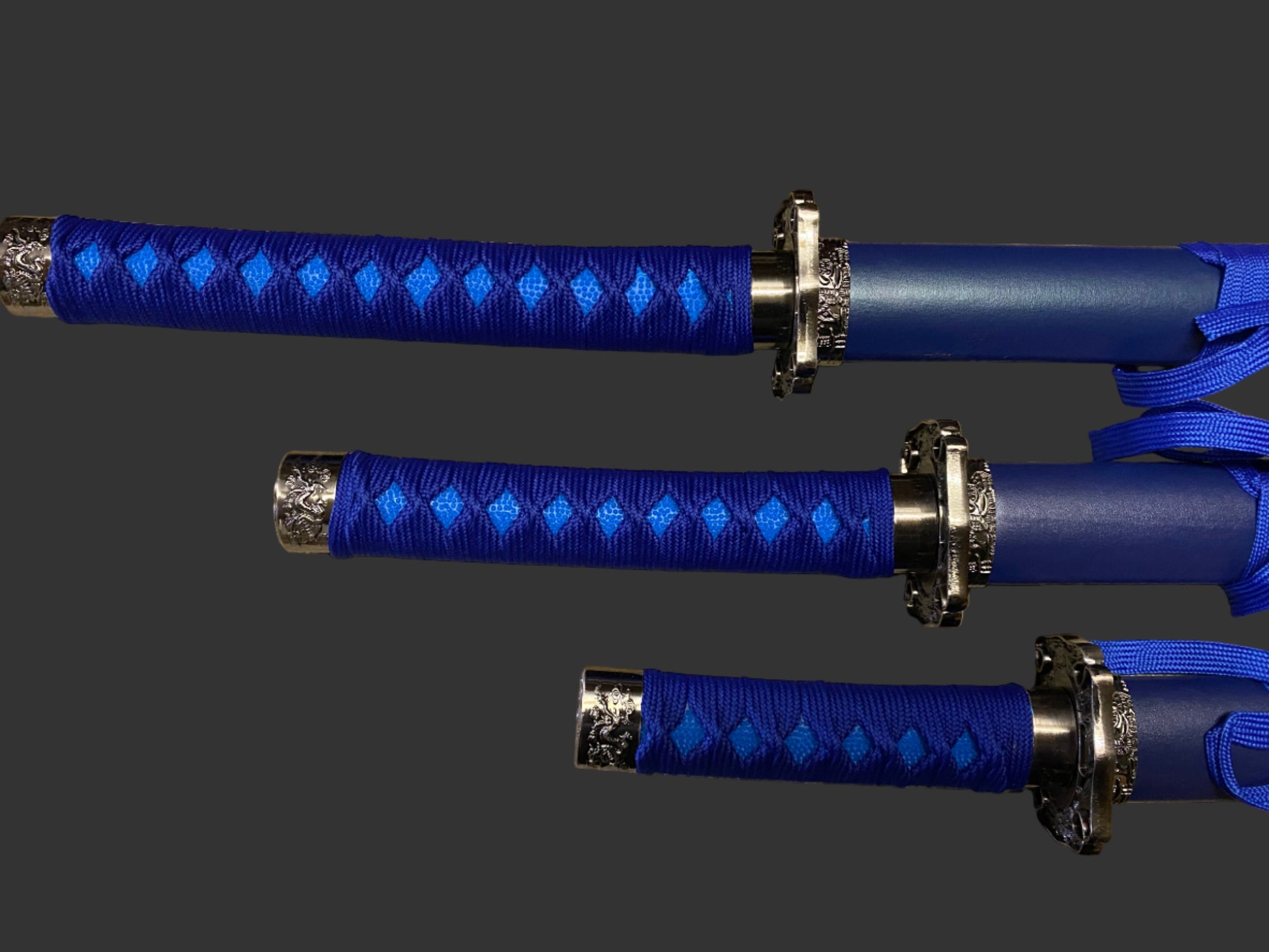 Three blue-handled samurai swords with decorative hilts on a gray background