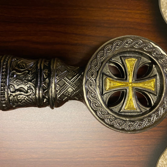 Decorative handle with intricate designs and a gold cross on a wooden background