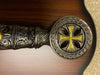 Decorative handle with intricate designs and a gold cross on a wooden background