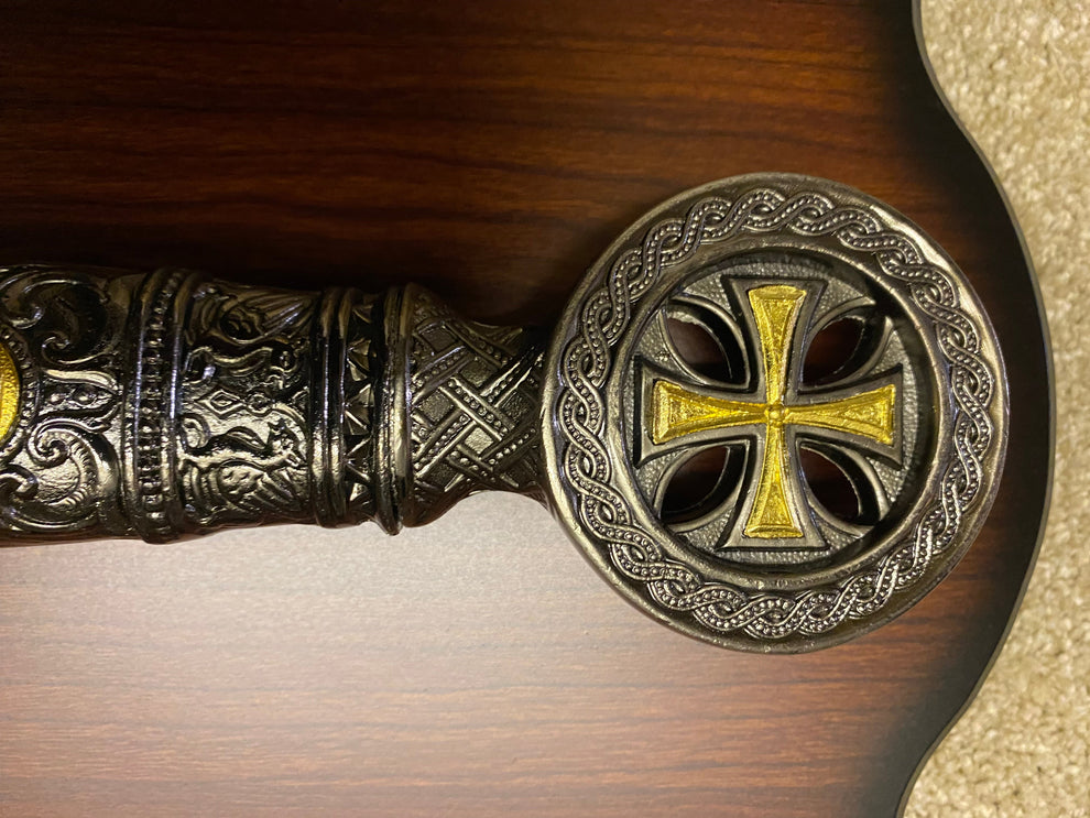 Decorative handle with intricate designs and a gold cross on a wooden background
