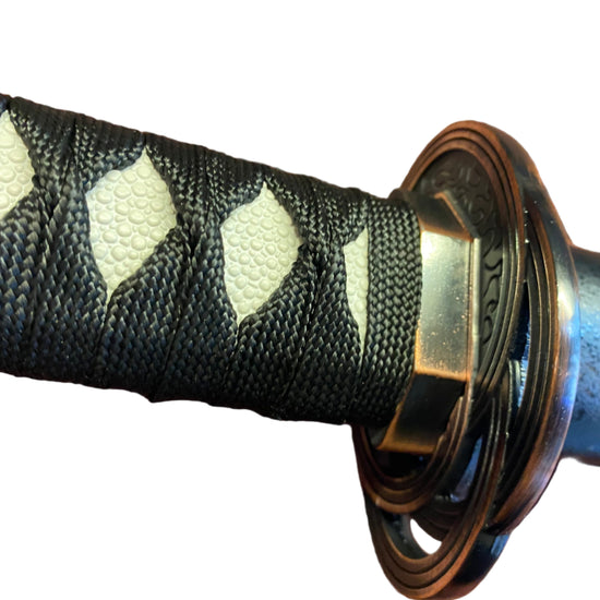 Close-up of a sword handle with black and white patterned grip and gold accents on a white background