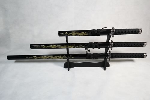 A set of three decorative dragon-themed Samurai swords with black handles and sheaths, displayed on a wooden stand against a white background.