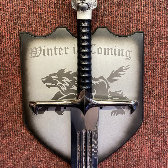 Decorative sword with a wolf head finial and 'Winter is Coming' text on a shield, against a textured brown background.