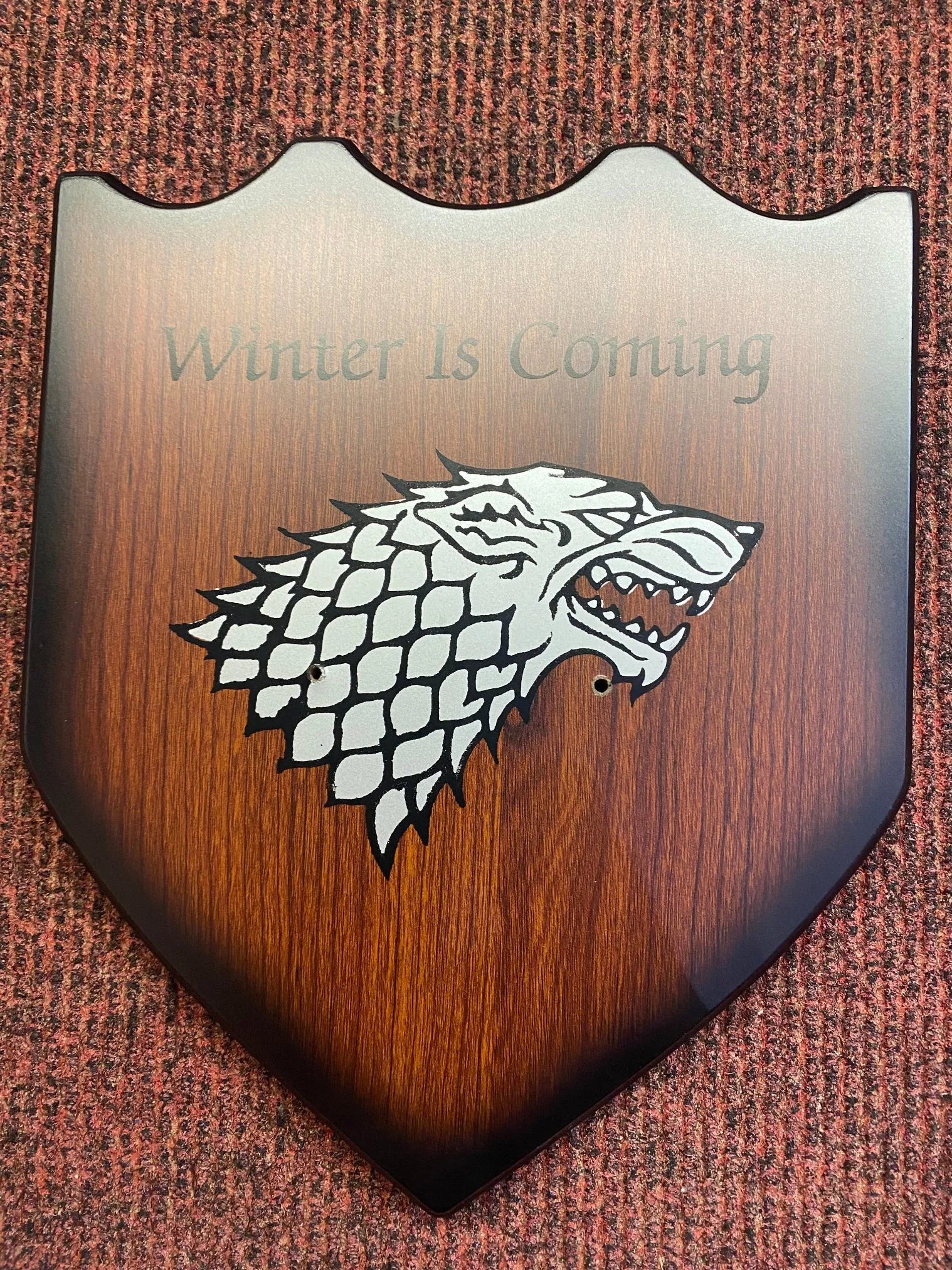 Wooden shield with a wolf head emblem and 'Winter Is Coming' text on a brown background