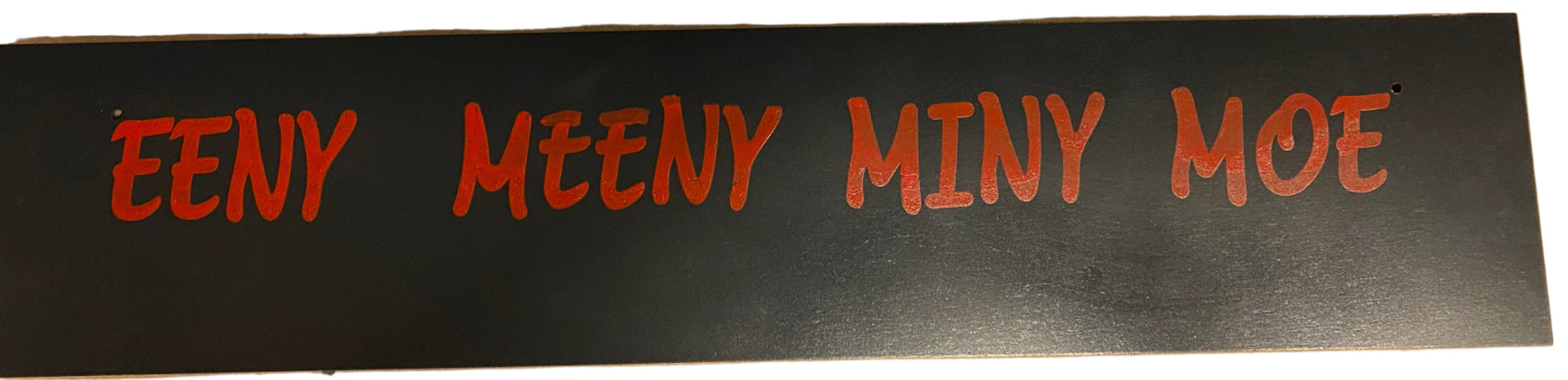 Strip of black material with red text 'EENY MEENY MINY MOE' on a white background