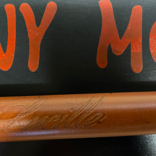 Wooden baseball bat with 'Lucchese' branding on a black background with orange text.
