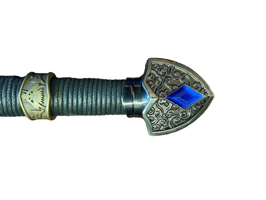 Decorative spear head with intricate designs and a blue gemstone on a white background