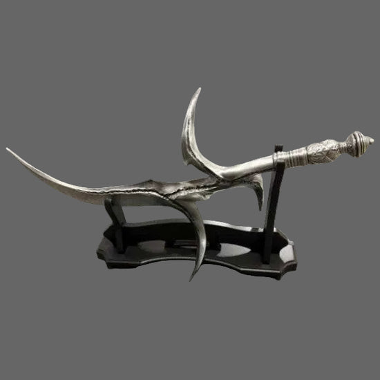 A decorative silver-colored curved sword or dagger displayed on a black stand, photographed on a gray carpeted floor with wood flooring visible in the background.