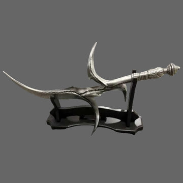A decorative silver-colored curved sword or dagger displayed on a black stand, photographed on a gray carpeted floor with wood flooring visible in the background.