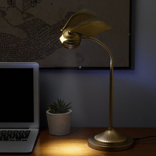 Gold desk lamp illuminating a laptop on a wooden surface with a plant in the background.