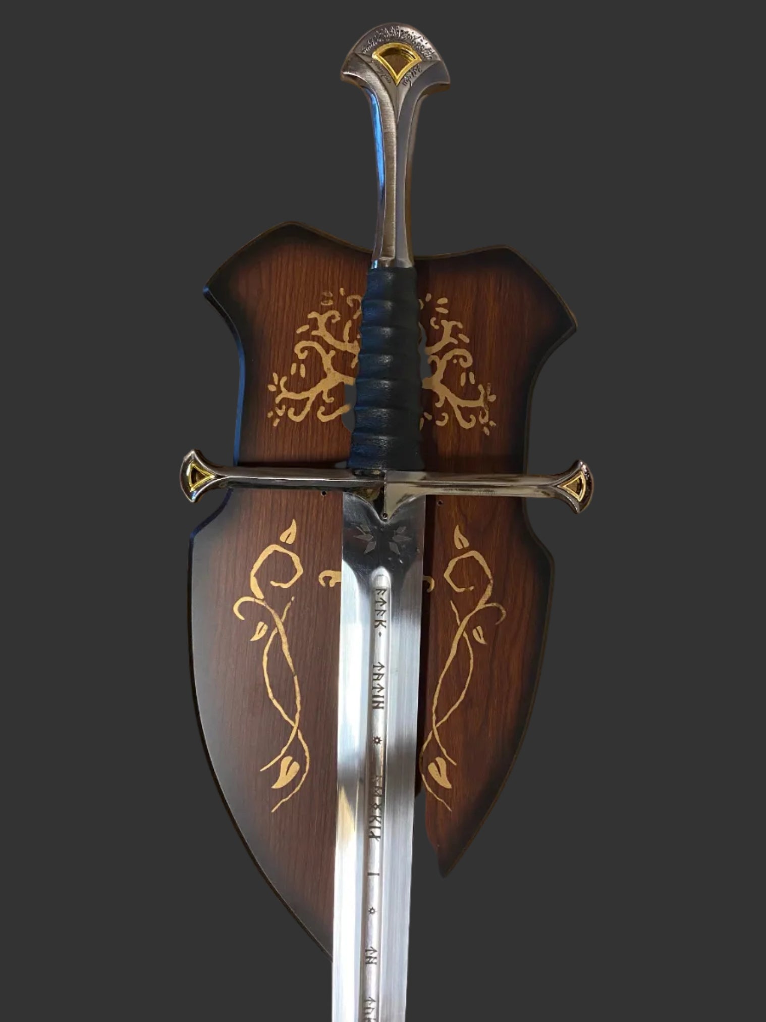 A decorative medieval-style sword with a polished silver blade, black wrapped hilt, and ornate gold detailing, shown alongside a matching dark brown wooden scabbard decorated with gold floral patterns.