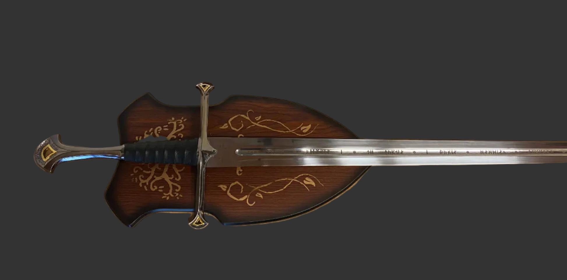A decorative medieval-style sword with a dark brown wooden scabbard featuring gold floral engravings, a silver blade, and a gold crossguard, shown against a solid dark gray background.