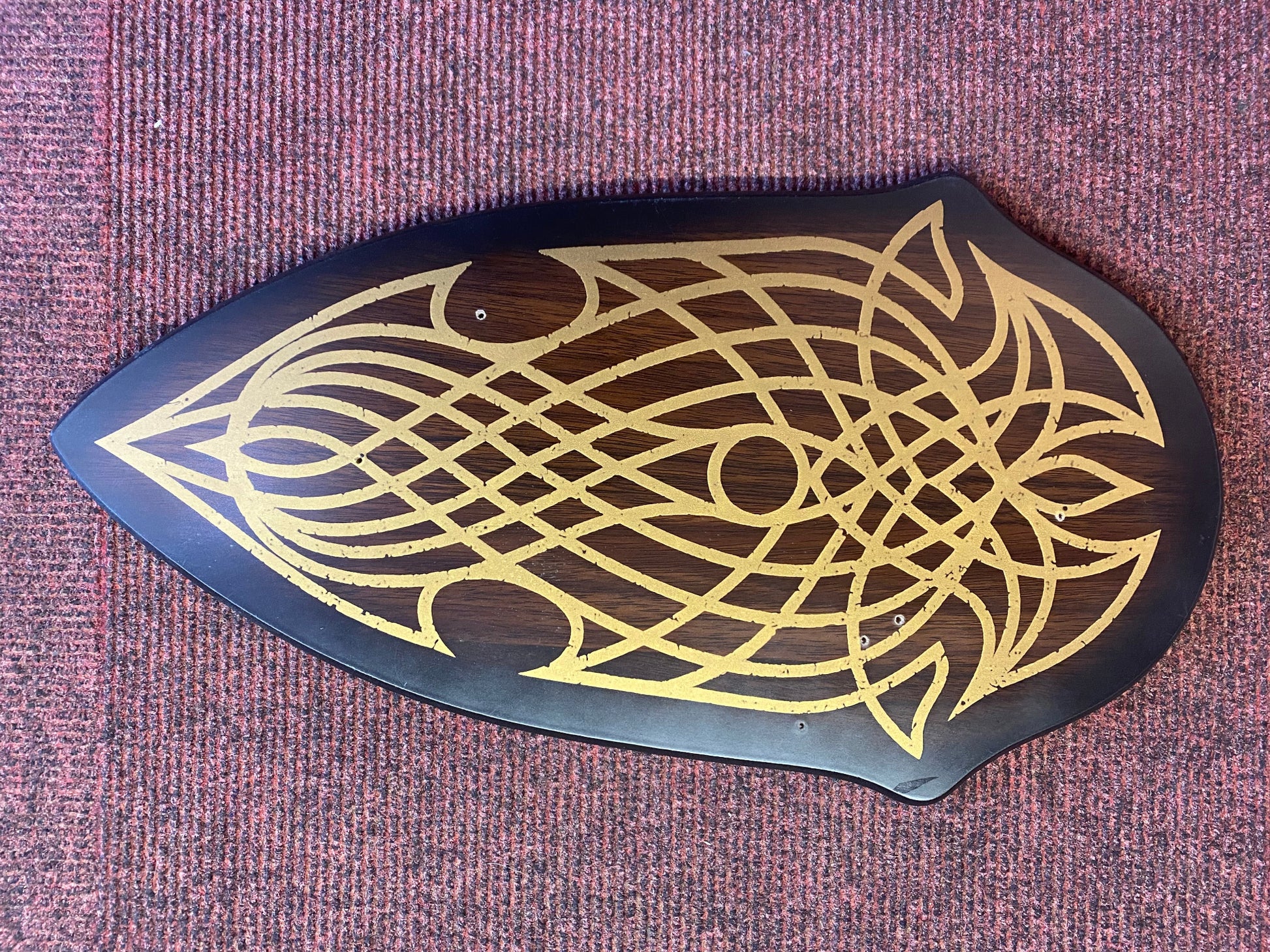Decorative wooden plaque with gold intricate design on a purple textured background