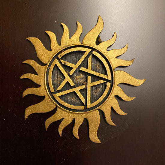 Gold sun-shaped symbol with a pentagram in the center on a dark background