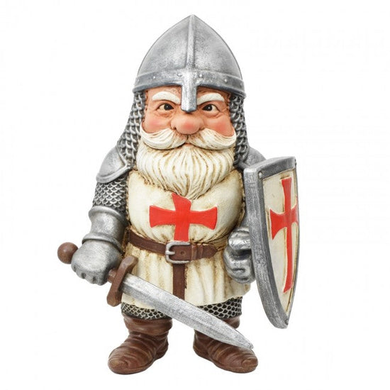 A small knight figurine wearing silver chainmail armor, a silver helmet, a cream tunic with a red cross, and brown boots, holding a sword and a shield. The figurine is photographed against a plain white background with a small logo in the bottom right corner.