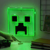 Green neon sign shaped like a character's face on a wall, with a hand touching it.