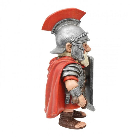 A small Roman soldier figurine shown in profile against a plain white background. The figure wears a silver helmet with a red crest, a red cape, silver armor, and brown sandals, and holds a shield and sword.