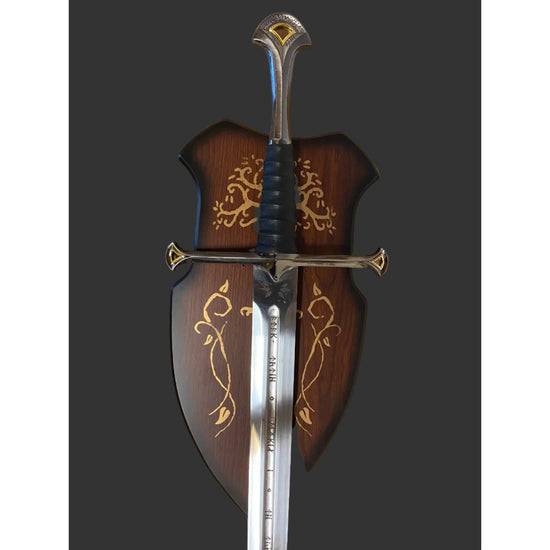 A decorative medieval-style sword with a polished silver blade, black wrapped hilt, and ornate gold detailing, shown alongside a matching dark brown wooden scabbard decorated with gold floral patterns.